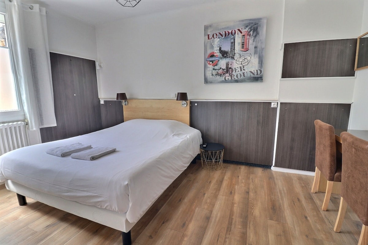A modern hotel room with a wooden floor, a bed with white linens, a round side table, and a wall-mounted artwork depicting London.