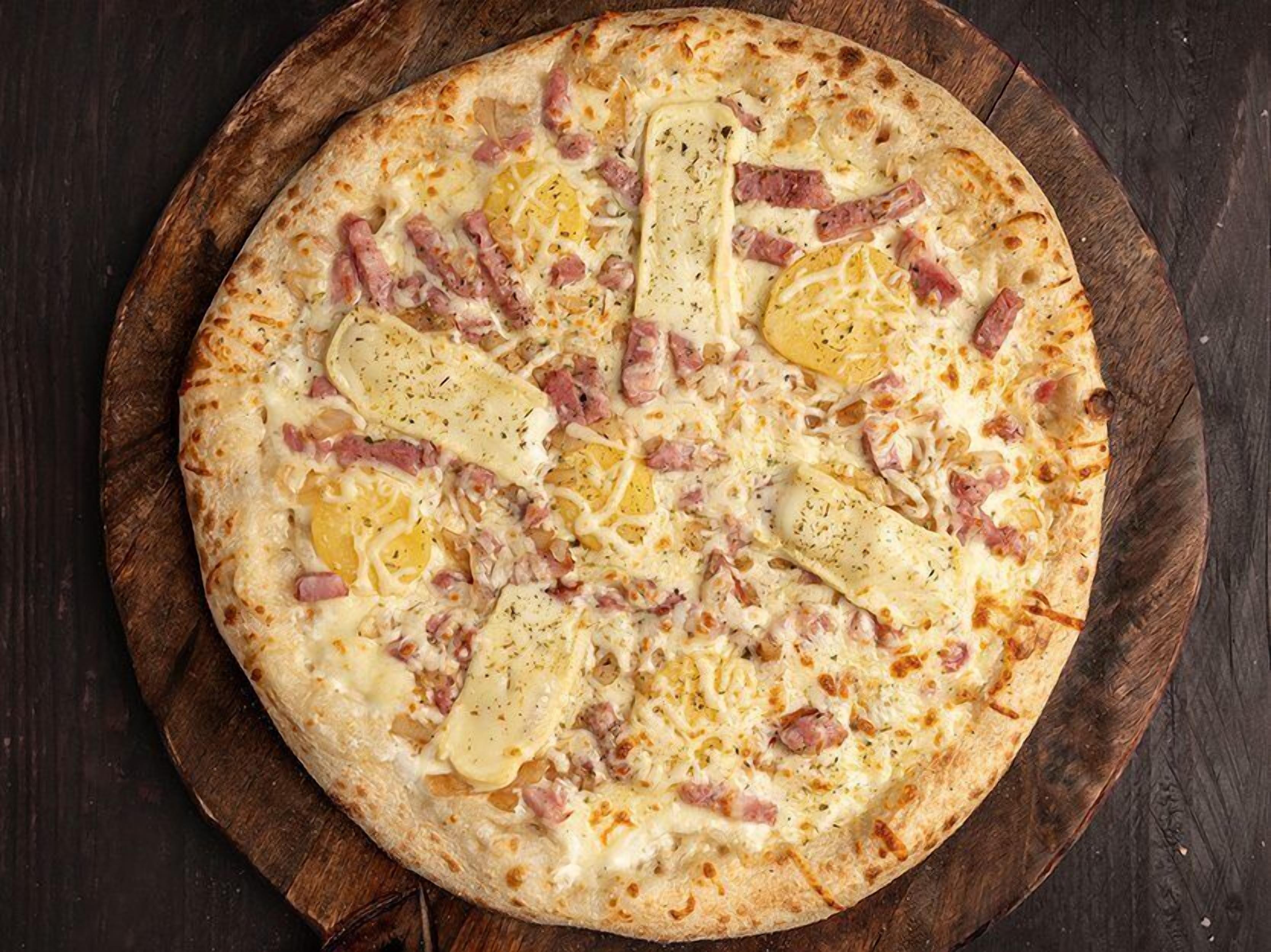 Una pizza con jamón y queso sobre una tabla de madera.