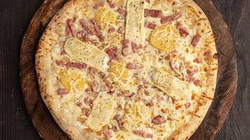 Una pizza con jamón y queso sobre una tabla de madera.