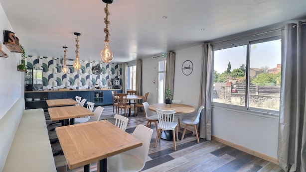 Un comedor moderno con mesas y sillas de madera, una cocina al fondo y ventanas amplias con vistas al exterior.