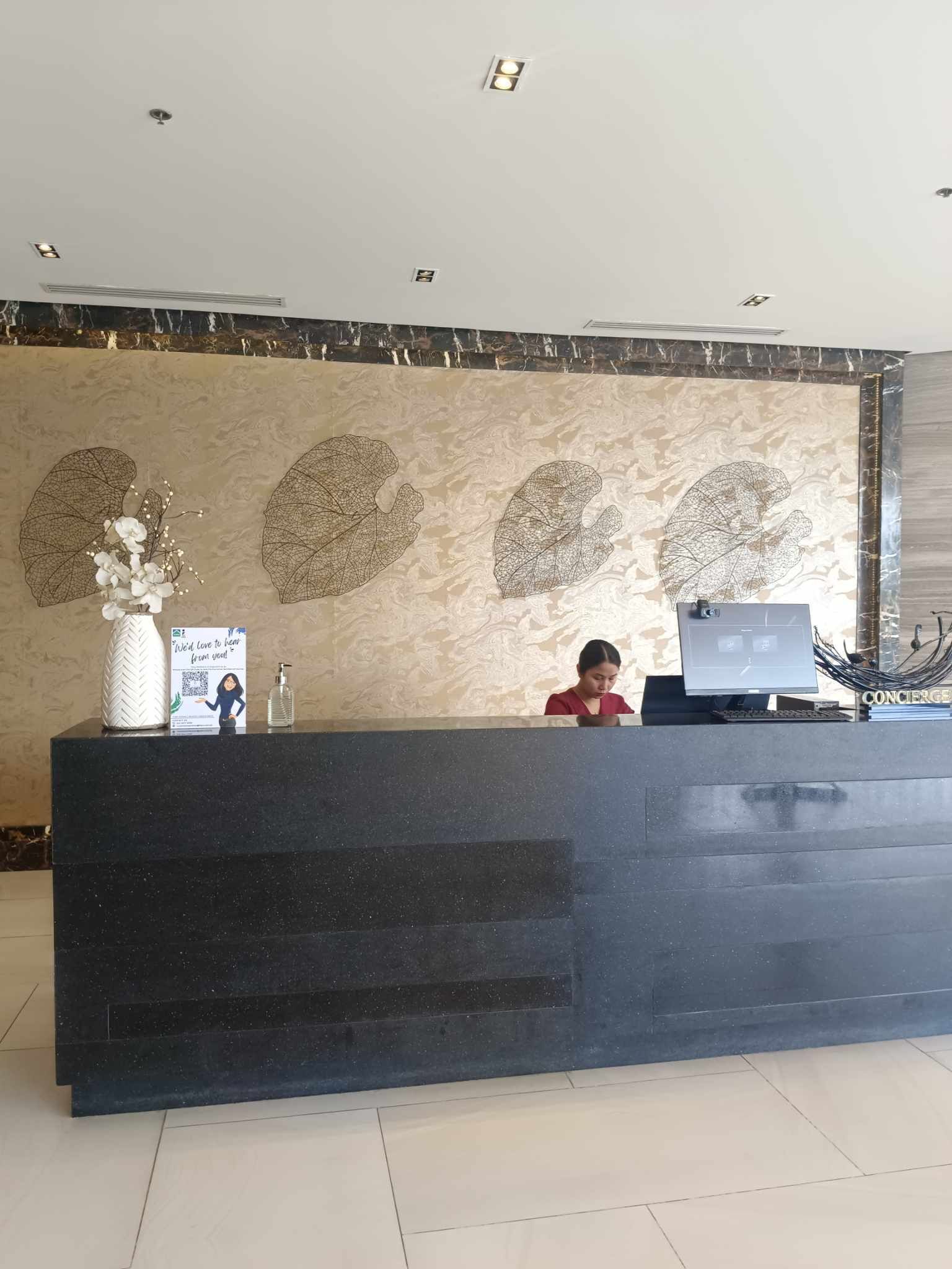 A reception desk with a marble-patterned wall, a vase with white flowers, and a laptop on the counter.