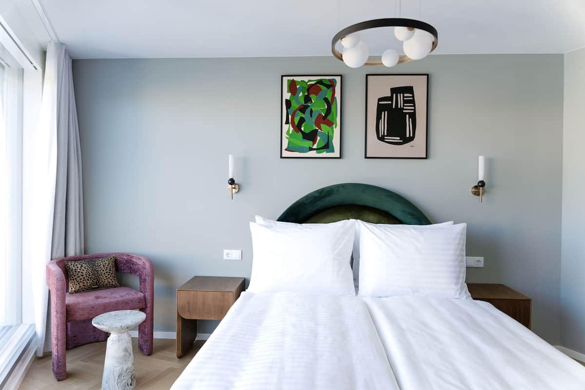 Ein modernes Schlafzimmer mit einem großen Bett, einem kleinen runden Tisch, einem violetten Sessel und zwei Wandlampen.