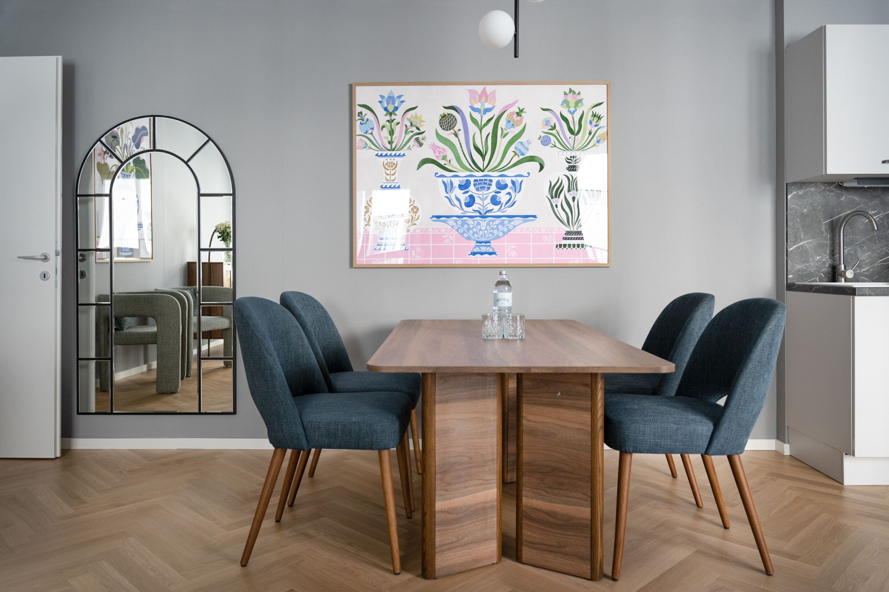 Ein Essbereich mit einem Holztisch, zwei blauen Stühlen und einem floralen Bild in einem Rahmen an der Wand.
