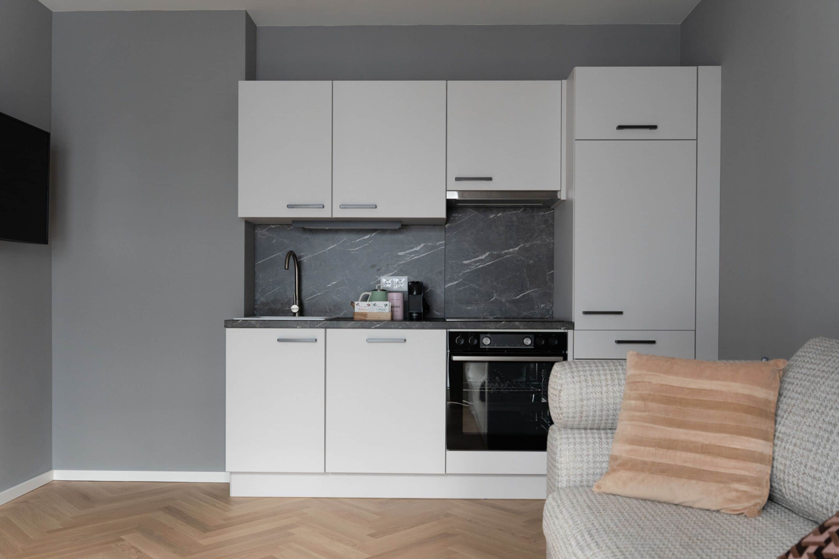 A modern kitchen with white cabinets, a marble backsplash, and a built-in oven.