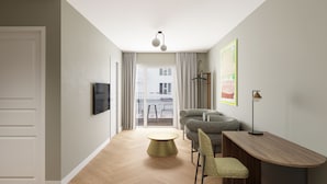 Una habitación moderna y bien iluminada con piso de madera, una mesa de comedor con sillas, un televisor montado en la pared y vistas a través de un amplio ventanal.