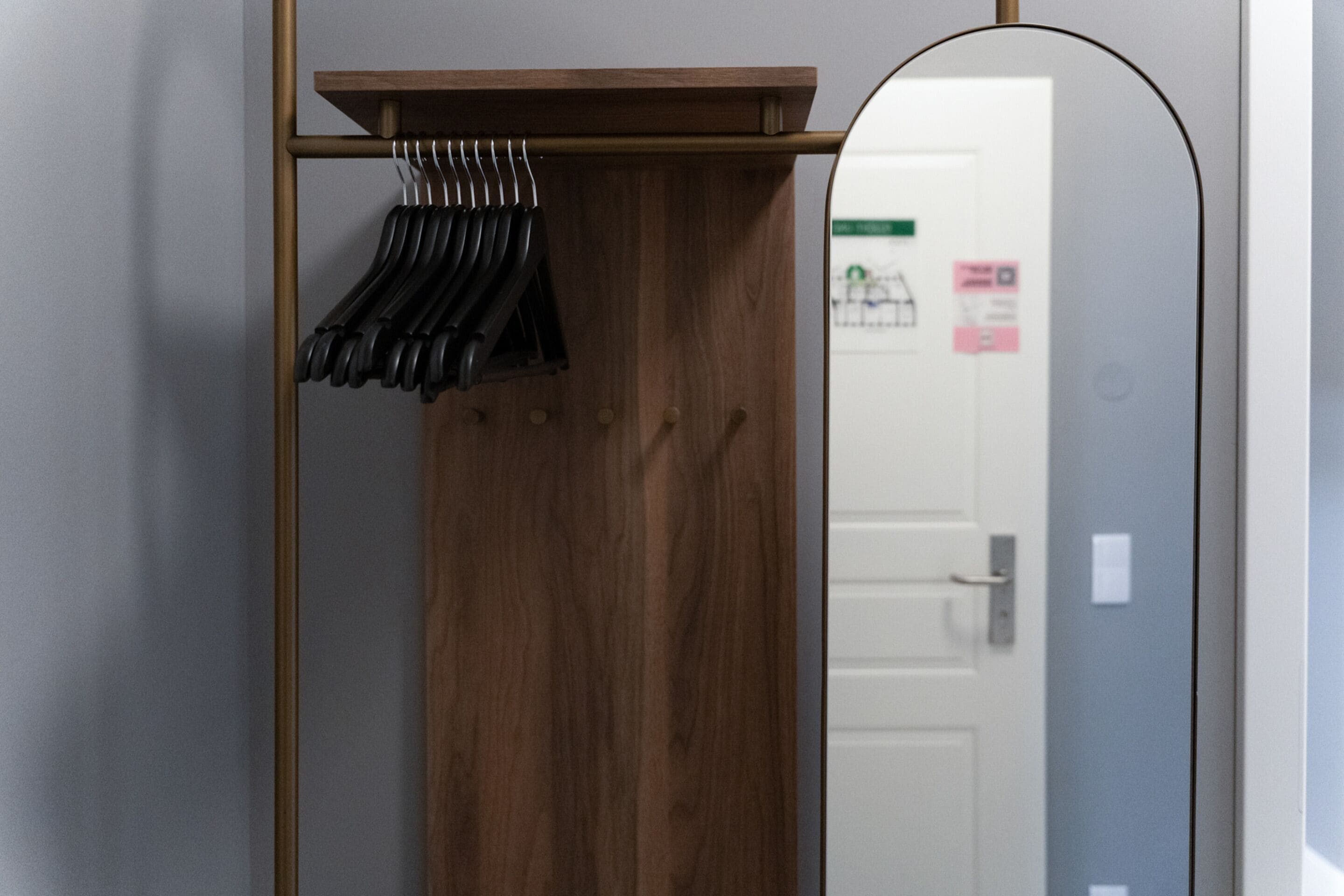 A wooden wardrobe with a mirror and a coat rack with black hangers.