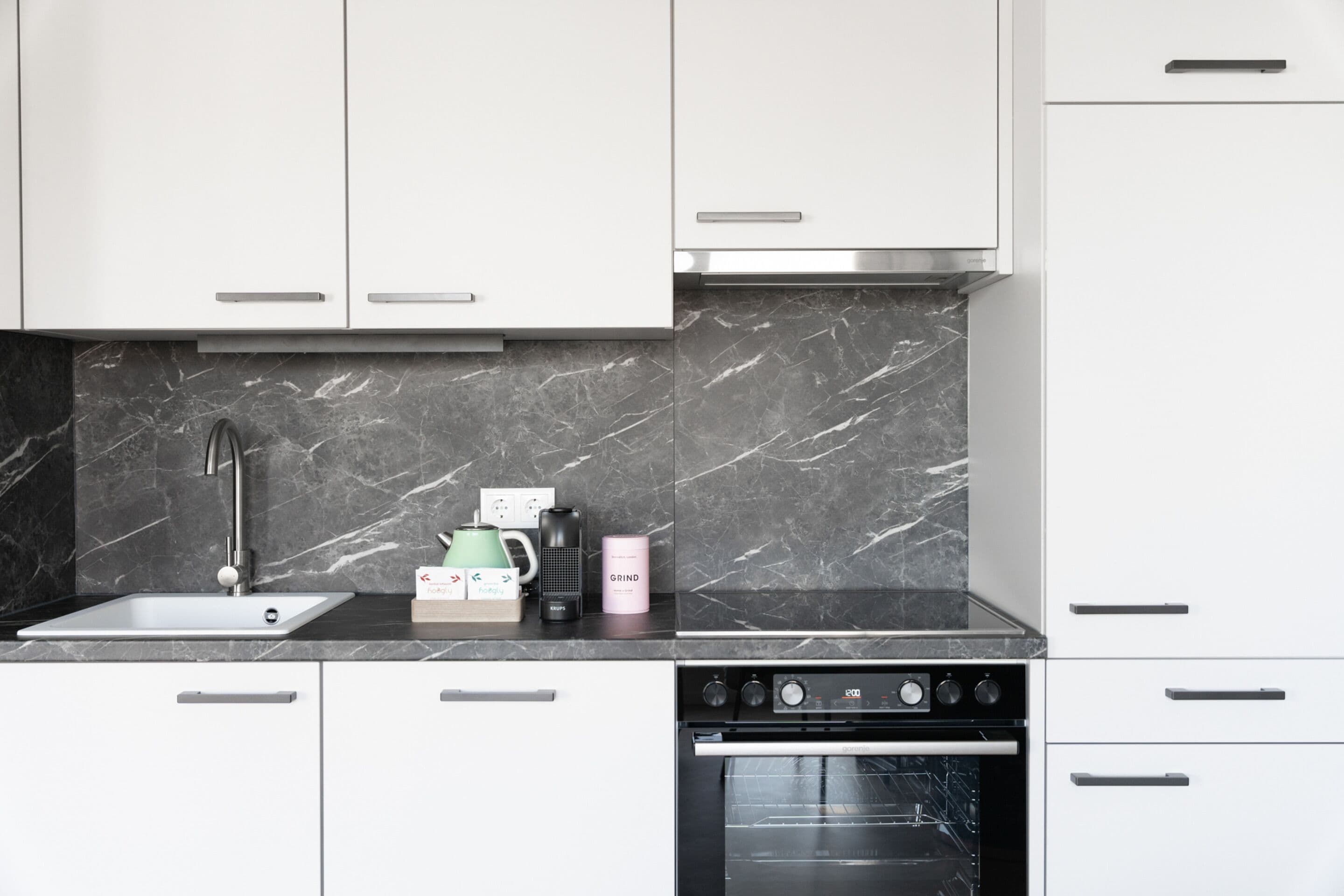 A modern kitchen with white cabinets, a marble backsplash, a built-in oven, and a coffee maker on the countertop.