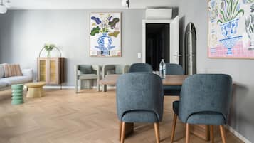 A modern living room with a dining area, featuring a wooden floor, grey upholstered chairs, a wooden dining table, and a sofa.