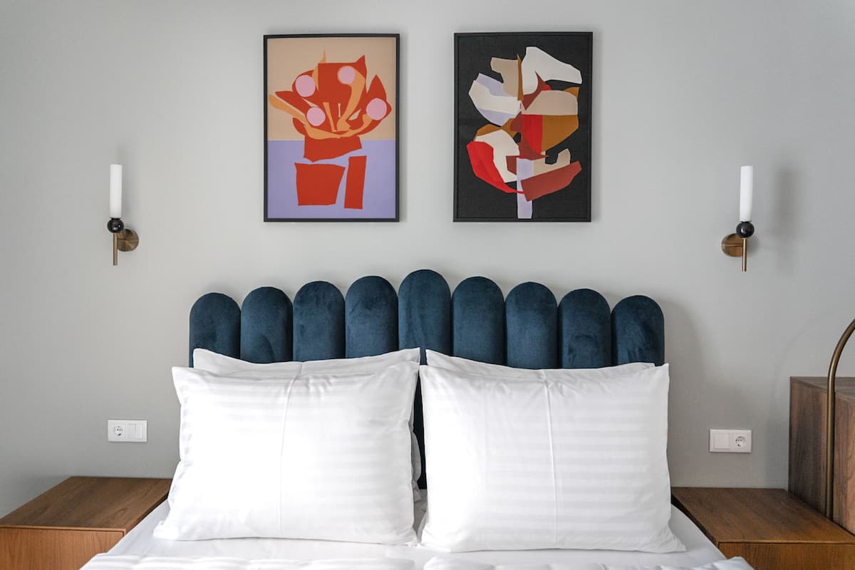 Ein Schlafzimmer mit einem Bett, zwei Kissen, einem Kopfteil und zwei abstrakten Gemälden an der Wand.