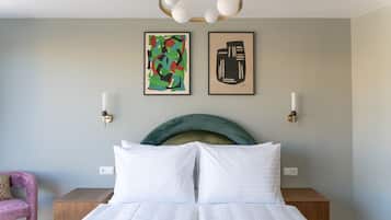 A modern hotel room with a large bed, two bedside tables, a headboard, and abstract artwork on the wall.