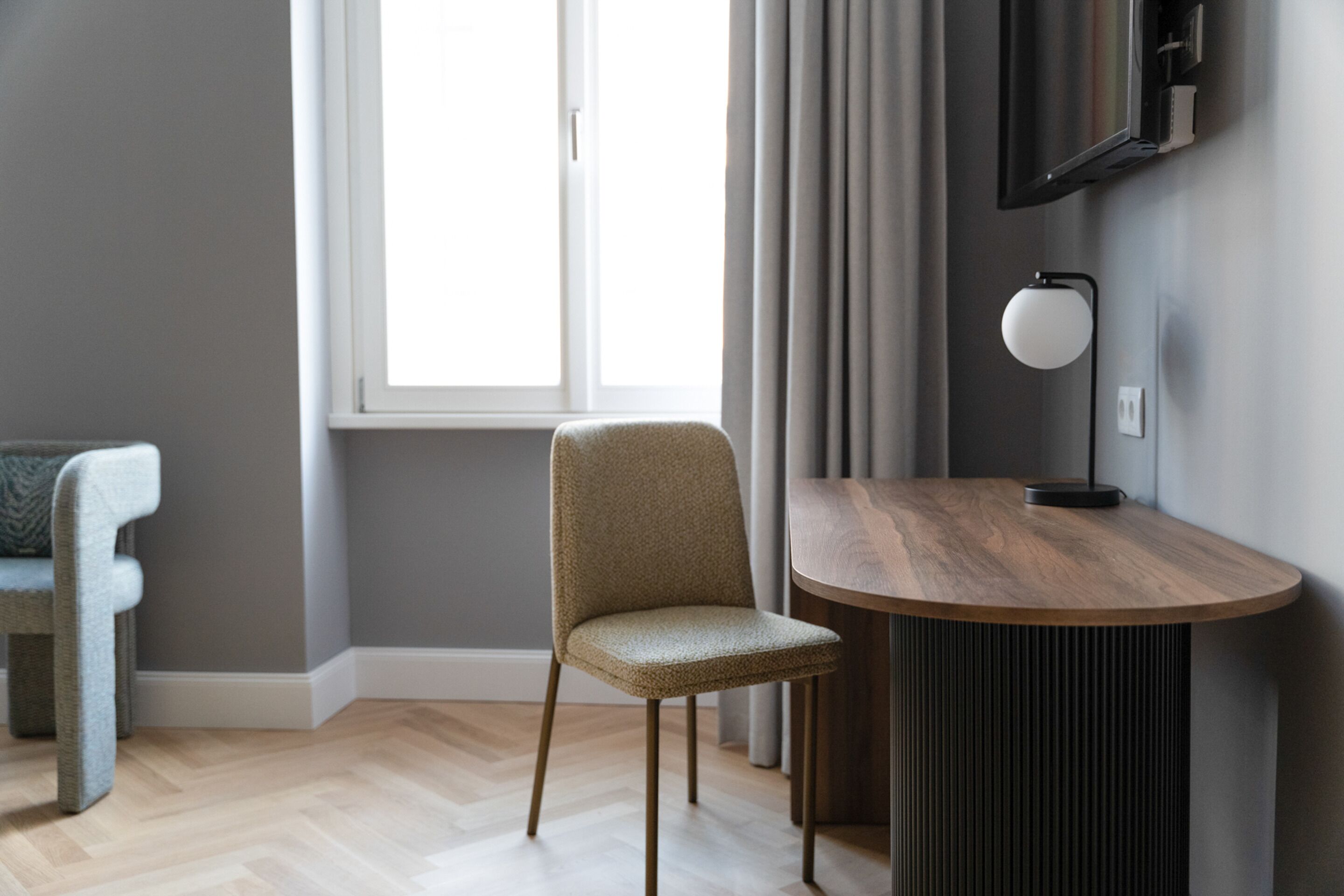 A modern room with a wooden dining table, a grey upholstered chair, and a television mounted on the wall.