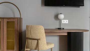 A modern room with a wooden desk, a patterned chair, a television mounted on the wall, and a lamp on the desk.