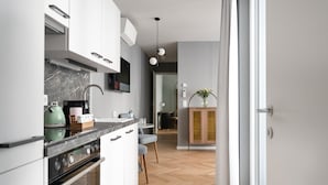 Una cocina moderna con armarios blancos, una encimera de mármol y un horno empotrado. Se distingue un área de comedor con una mesa y sillas al fondo.