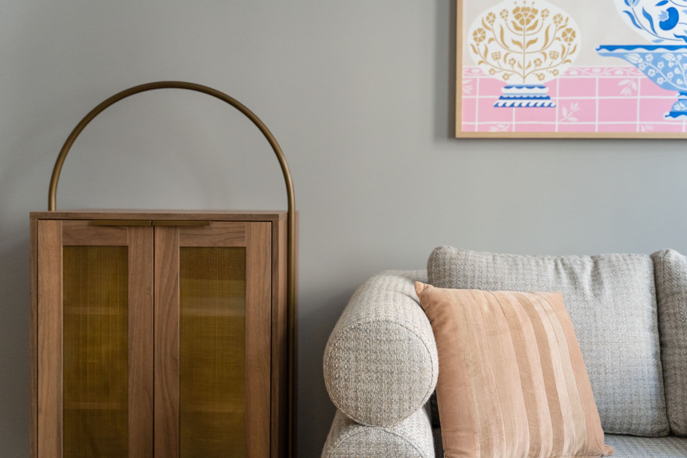 A wooden cabinet with a glass door, a grey sofa with striped cushions, and a framed artwork on the wall.