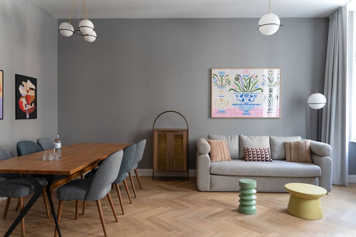 Ein modernes Wohnzimmer mit einem Holzesstisch, grauen Sofas und einem farbenfrohen abstrakten Gemälde an der Wand.