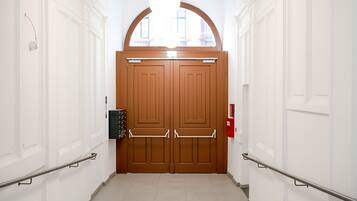A hallway with a double wooden door, white walls, and a tiled floor.