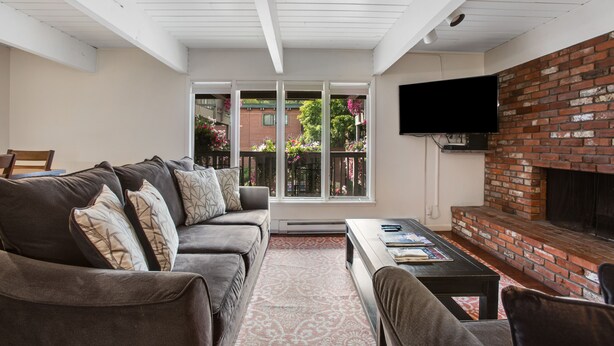 A living room with a brick fireplace, a sofa with cushions, a coffee table, and a TV mounted on the wall.