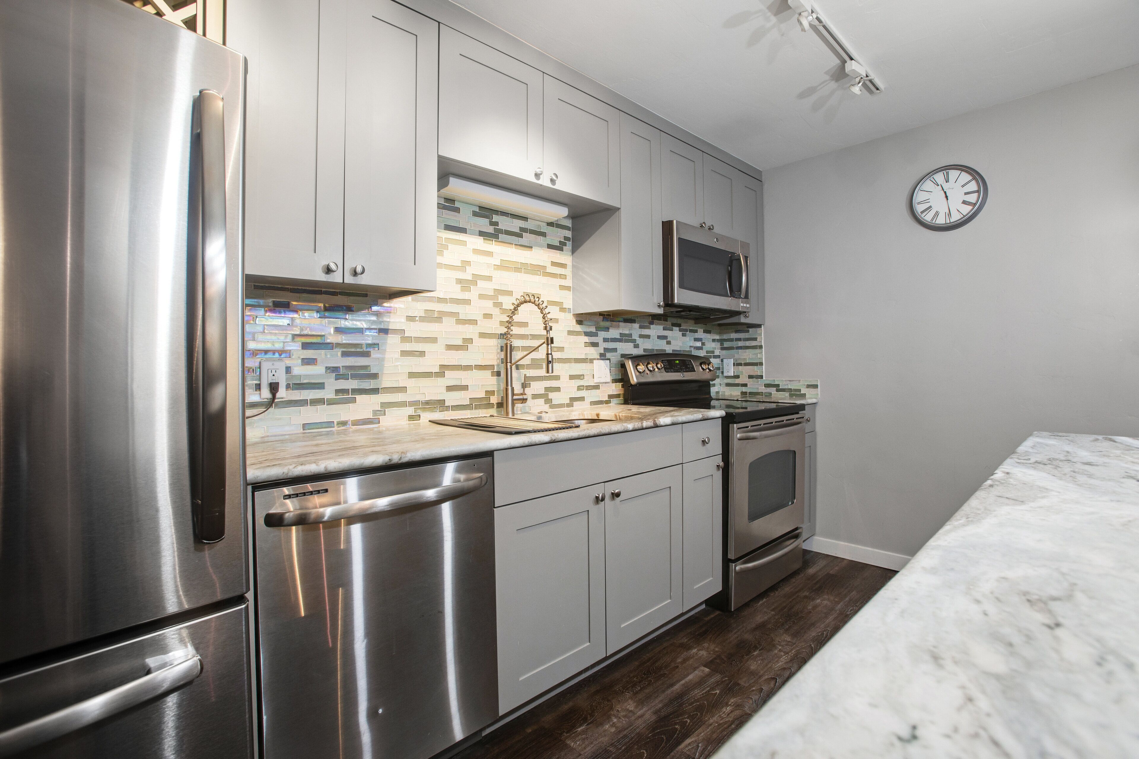 A modern kitchen with stainless steel appliances, a microwave, and a clock on the wall.