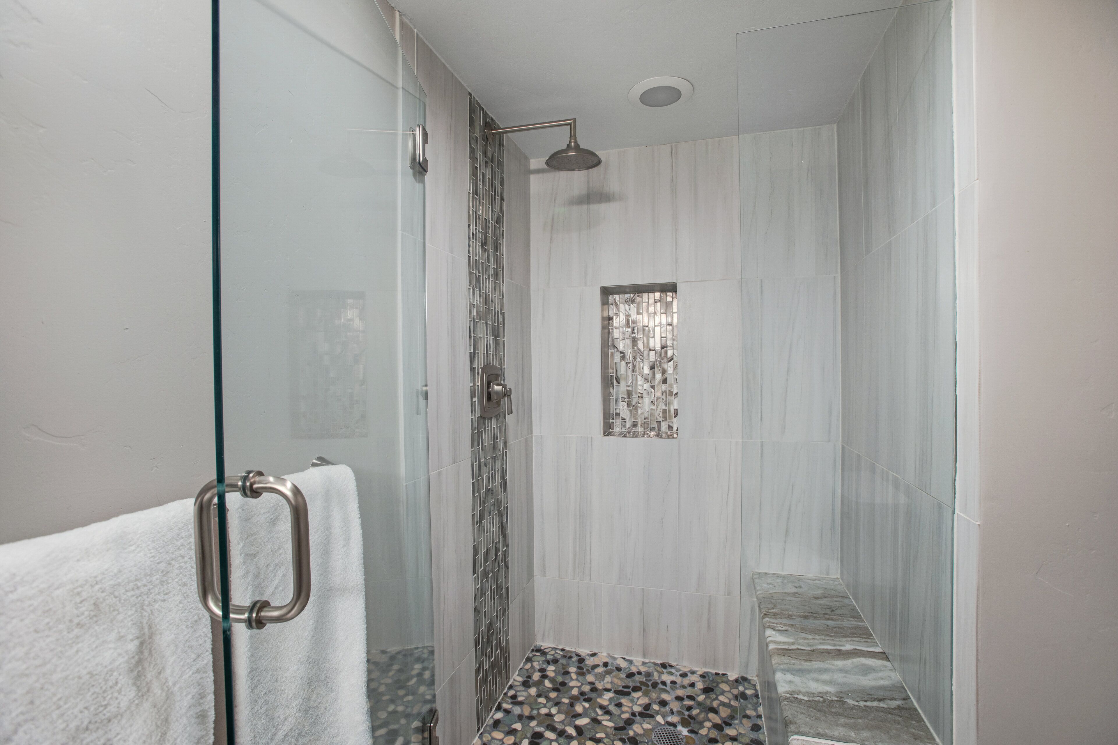 A modern bathroom with a glass shower enclosure, a white towel, and a patterned floor.