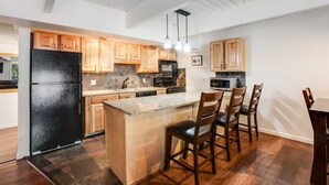 A modern kitchen with wooden cabinets, a black refrigerator, a granite countertop, and a dining area with chairs.
