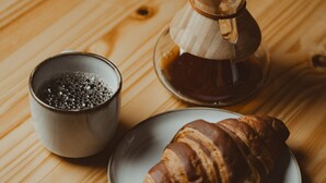 Una mesa de madera con una cafetera, una taza de café y un croissant.