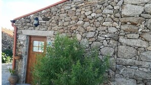 A stone building with a wooden door and a small garden area with potted plants.