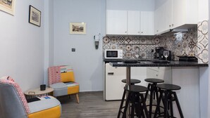 Een compacte keuken met een magnetron, koffiezetapparaat en barstoelen. Er zijn twee stoelen met kleurrijke bekleding en een kleine tafel.
