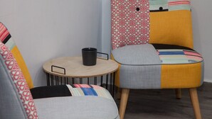 Twee stoelen met kleurrijke stoffen bekleding en een klein rond tafeltje met een zwarte mok.