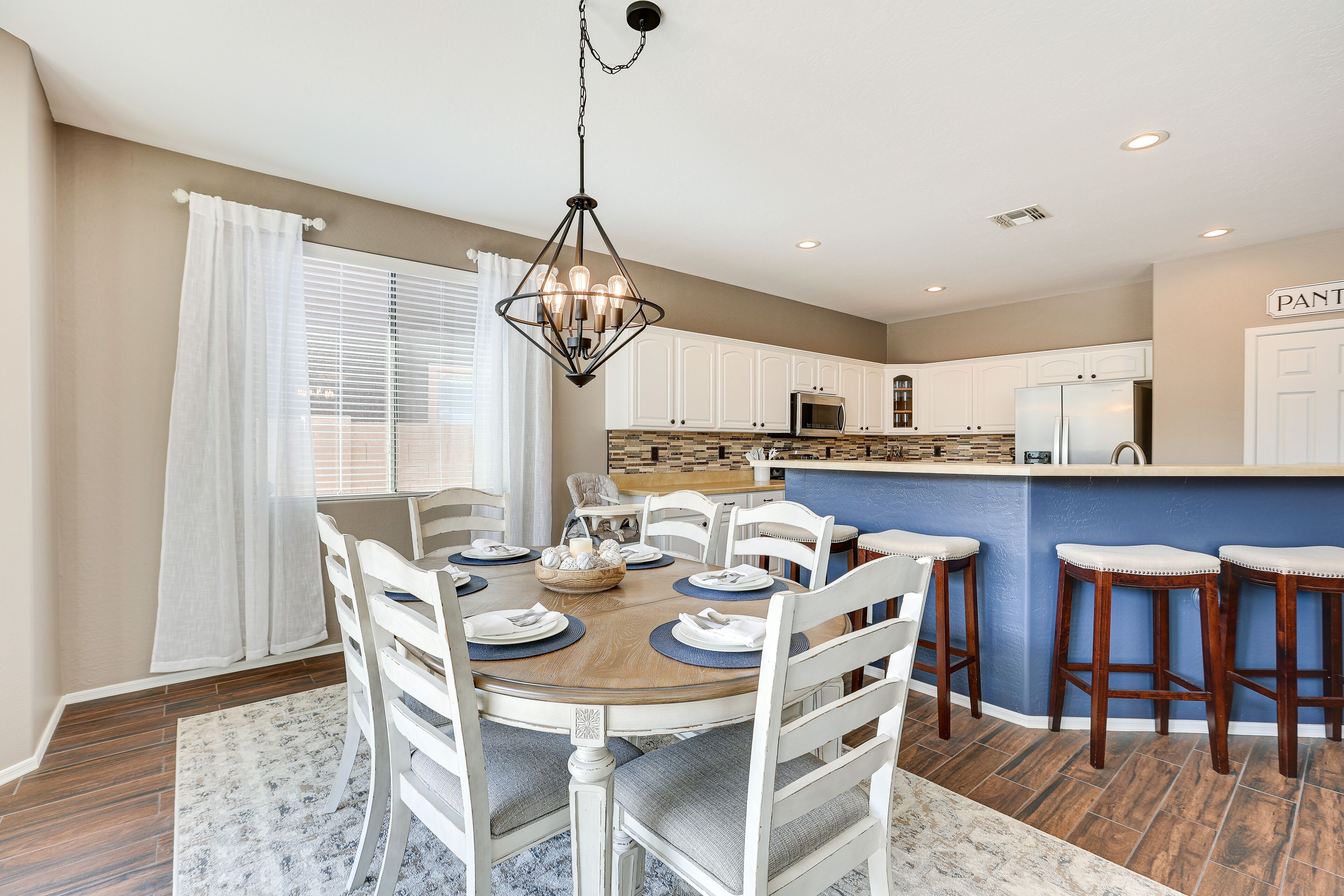 A modern kitchen with white cabinets, a blue island, and a dining area with a round table and chairs.