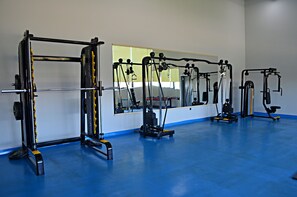 A gym with various exercise equipment, a large mirror, and a blue floor. - Arena Sport Hotel (Quba)