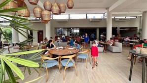A spacious indoor area with round tables and chairs, large windows, and hanging wicker lamps. - Flat com piscina privativa em Pipa (Tibau do Sul)