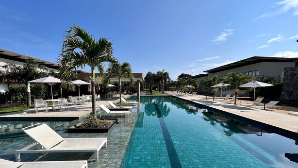 A pool area with lounge chairs, umbrellas, and palm trees. - Flat com piscina privativa em Pipa (Tibau do Sul)