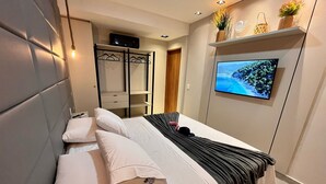A hotel room with a bed, a TV, a wardrobe, and a shelf with decorative items. - Flat com piscina privativa em Pipa (Tibau do Sul)