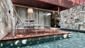 A pool area with a tiled floor, a seating area with chairs, and a stone wall. - Flat com piscina privativa em Pipa (Tibau do Sul)
