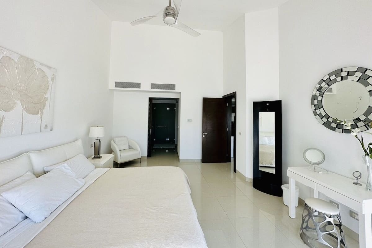 A modern hotel room with a large bed, a desk, a chair, a mirror, and a ceiling fan.