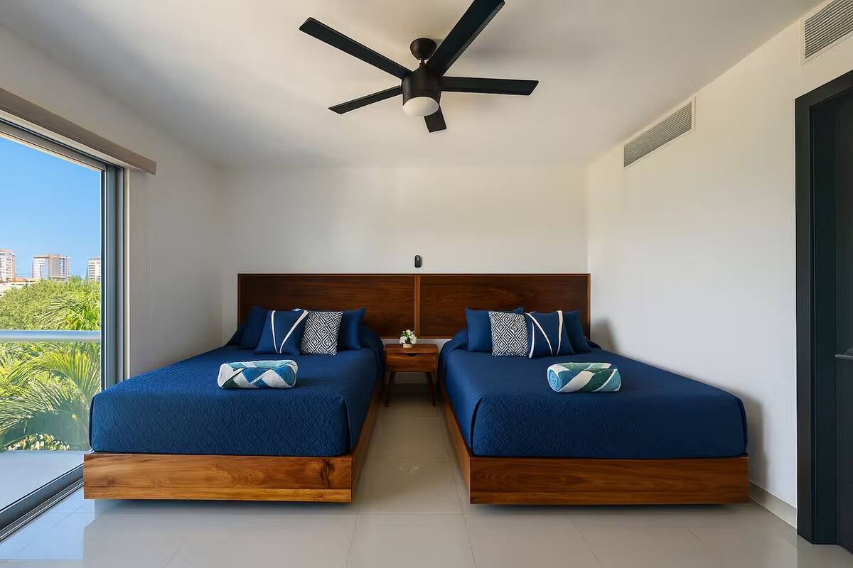 A modern bedroom with two beds, a ceiling fan, and a view of the city.