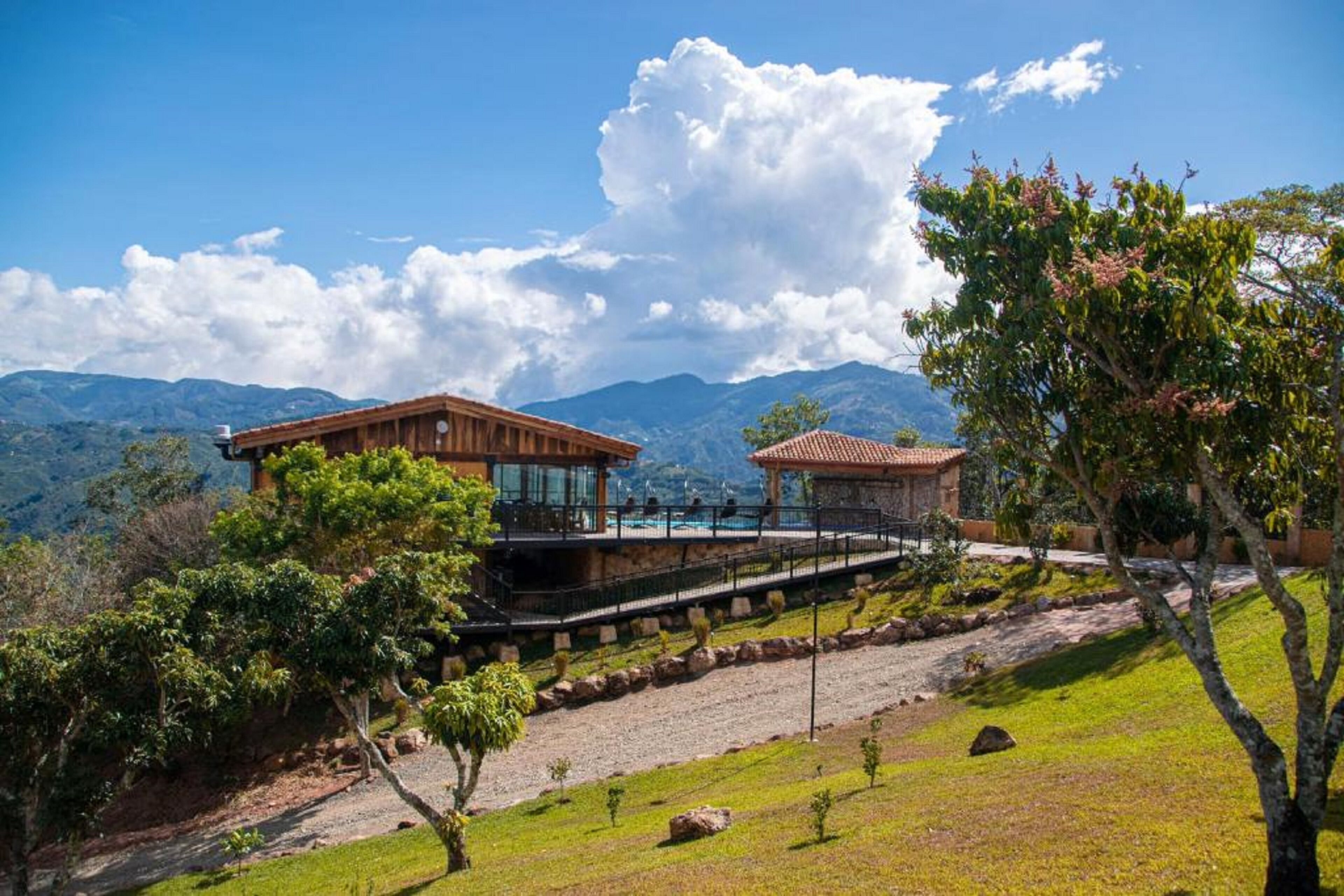 Una casa de dos pisos con piscina, rodeada de exuberante vegetación y montañas al fondo.