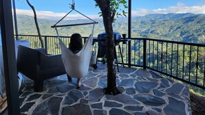 Uma cadeira balanço em rede pendurada em estrutura metálica, com vista para uma paisagem montanhosa.