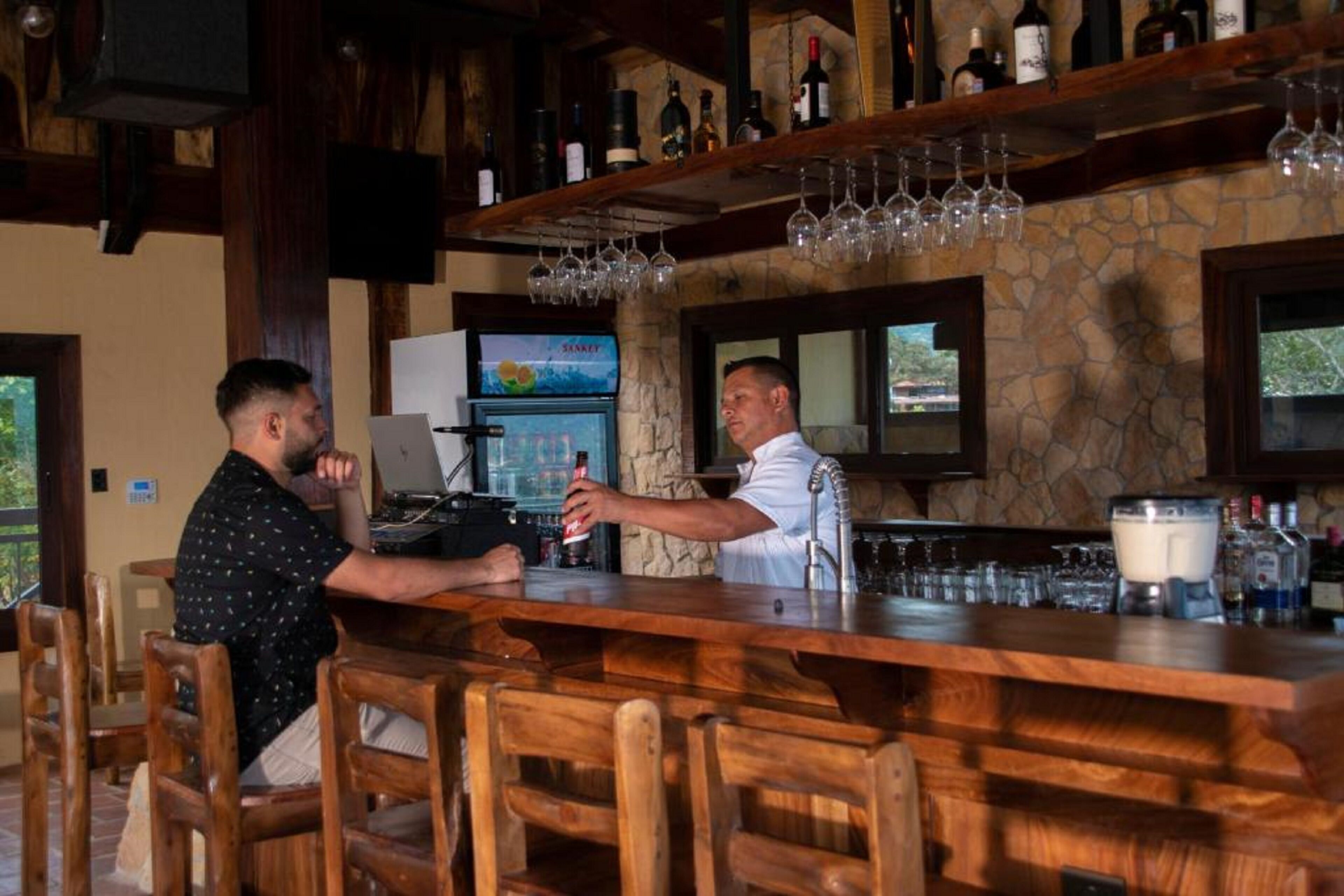 Zona de bar con mobiliario de madera, pared de piedra y un televisor que muestra un canal deportivo.