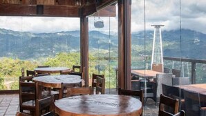 Interior em madeira com mesas e cadeiras redondas, amplas janelas com vista para as montanhas.