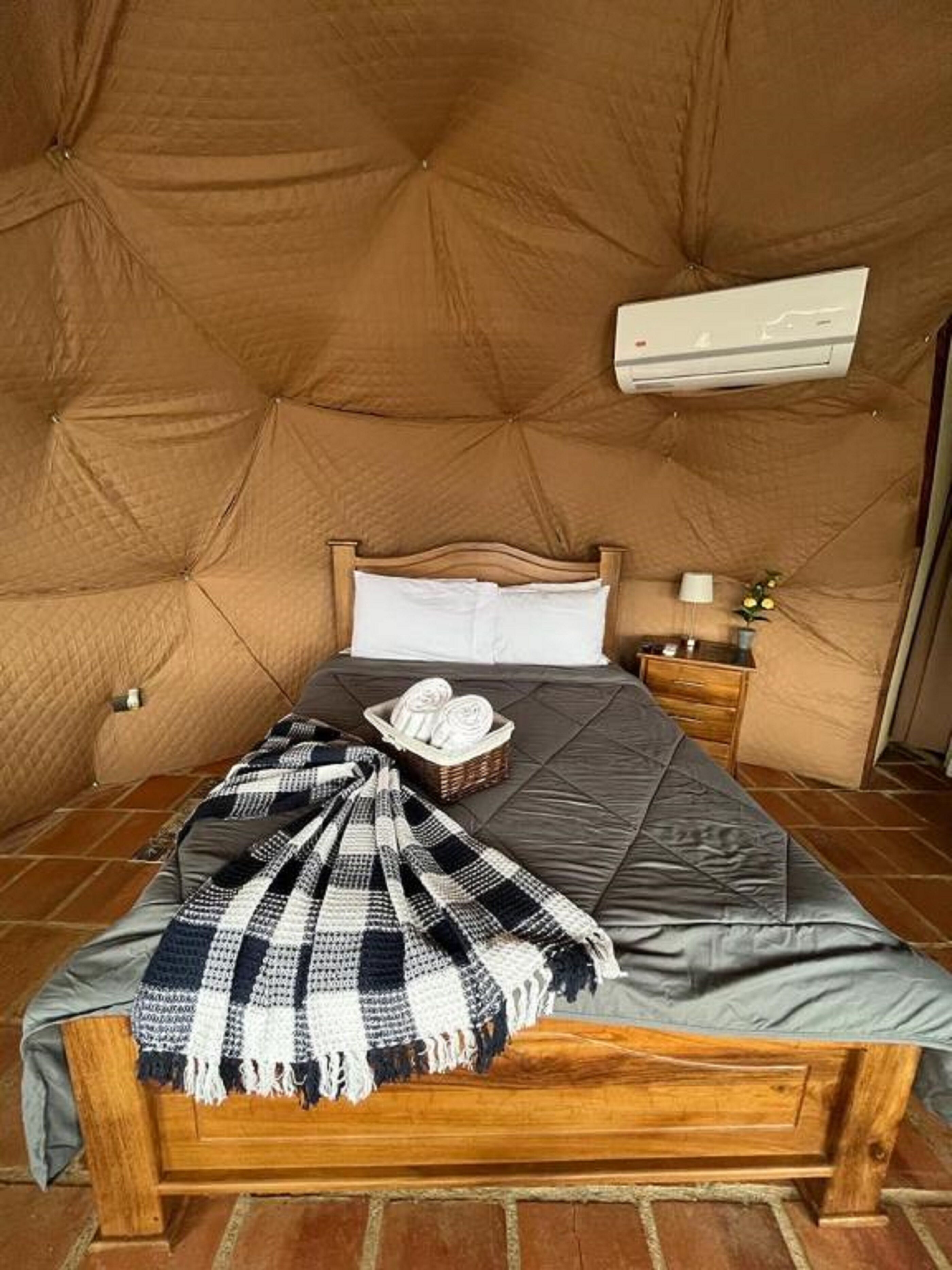 Ein gemütliches Zimmer mit einem großen Bett, einem Holz-Kopfschild, einem kleinen Nachttisch und einer Wand-Klimaanlage.