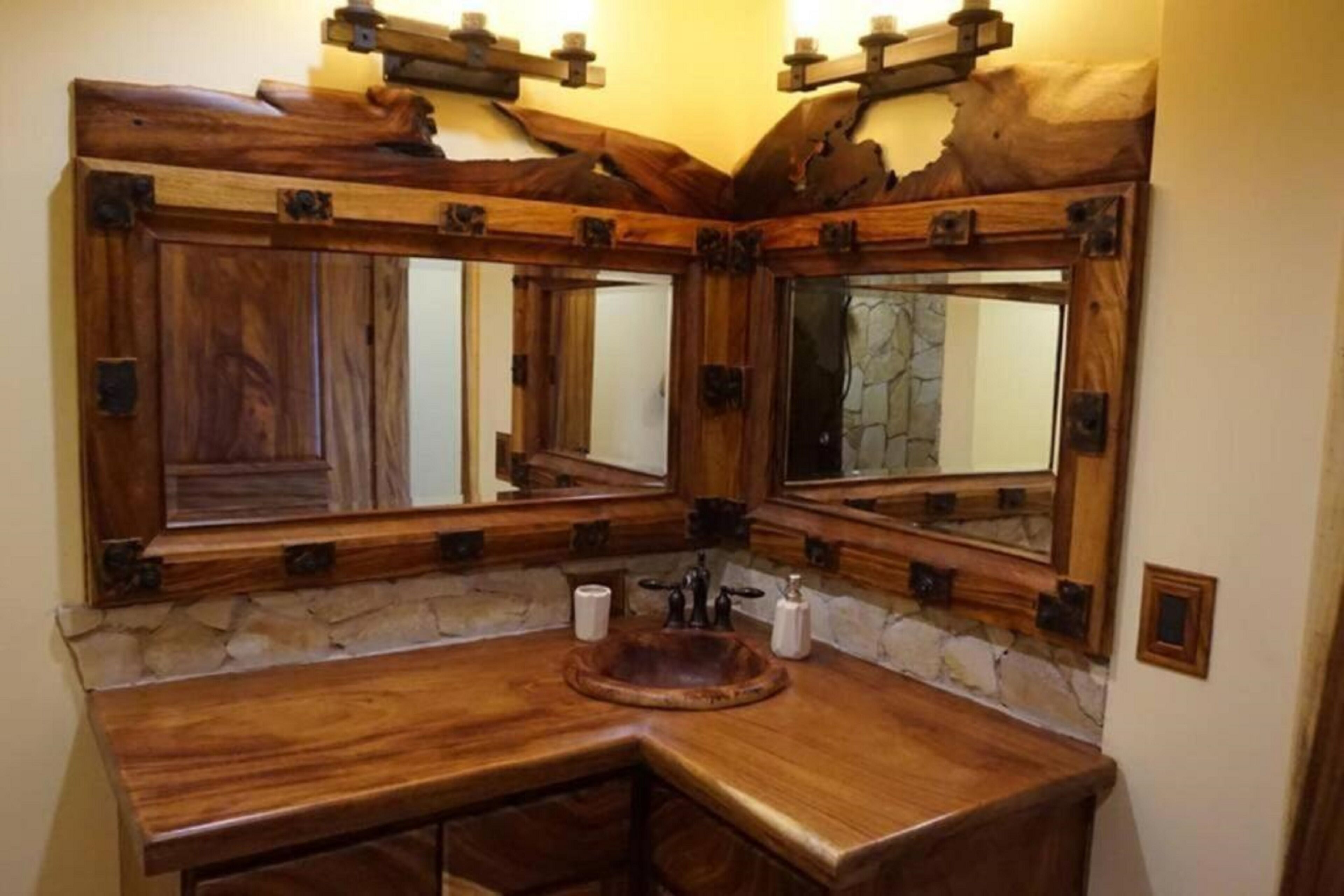 A bathroom with a wooden vanity, a stone backsplash, and a large mirror with wooden frames.