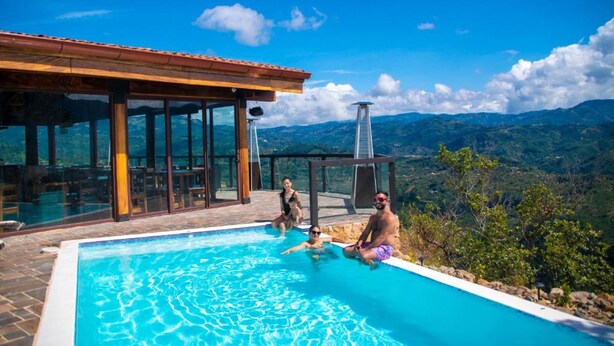 Piscina com vista para montanhas, área de estar coberta e estrutura envidraçada.