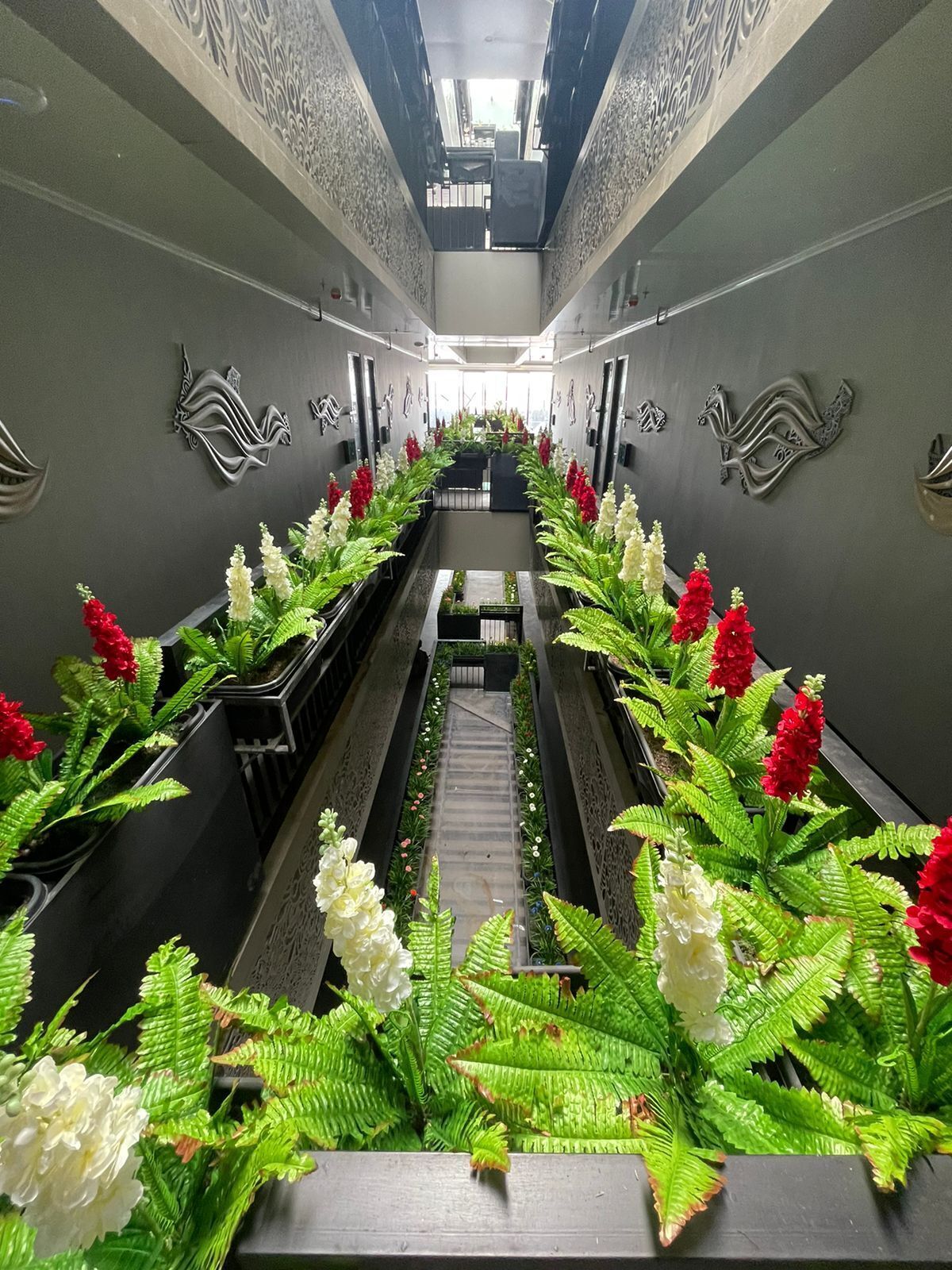 A corridor with a central walkway flanked by potted plants and decorative wall elements.