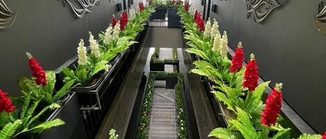 A corridor with a central walkway flanked by potted plants and decorative wall elements.