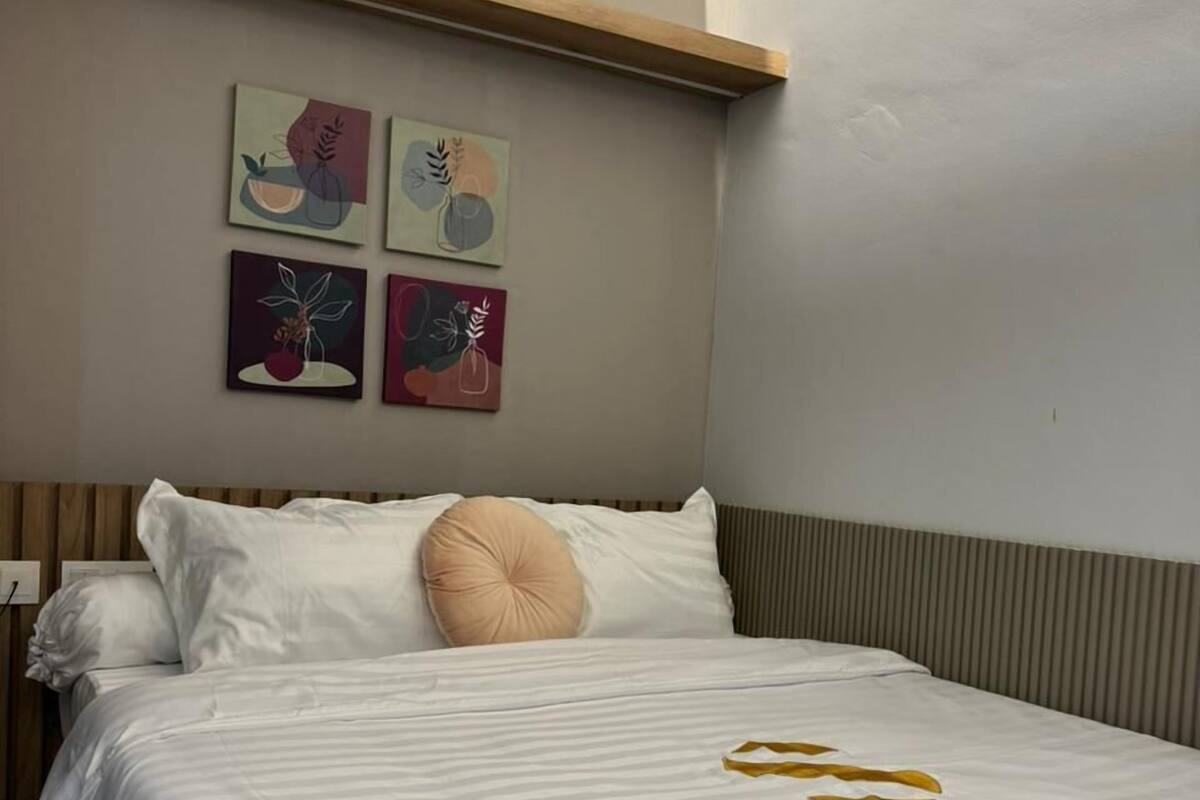 A neatly made bed with white and striped bedding, a wooden headboard, and a beige pillow. There are four framed artworks on the wall above the bed.