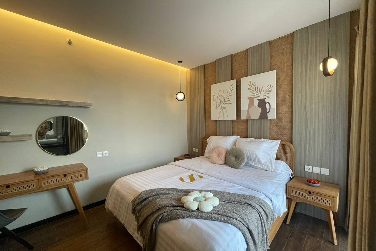 A modern bedroom with a large bed, bedside tables, a mirror, and artwork on the wall.