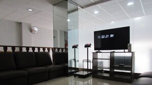 Een moderne wachtruimte met een zwarte leren bank, een glazen scheidingswand, een digitale klok en een televisie op een standaard.