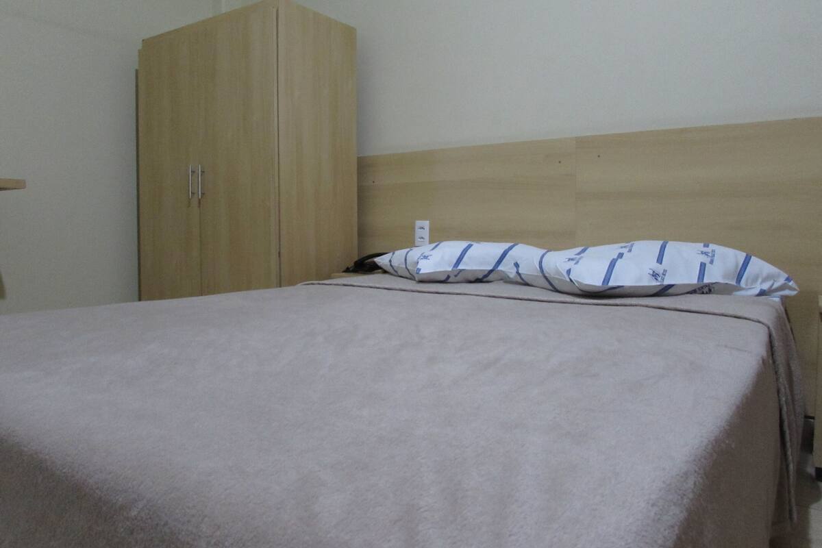 Une pièce comprenant un lit, une armoire en bois et une prise de courant murale.