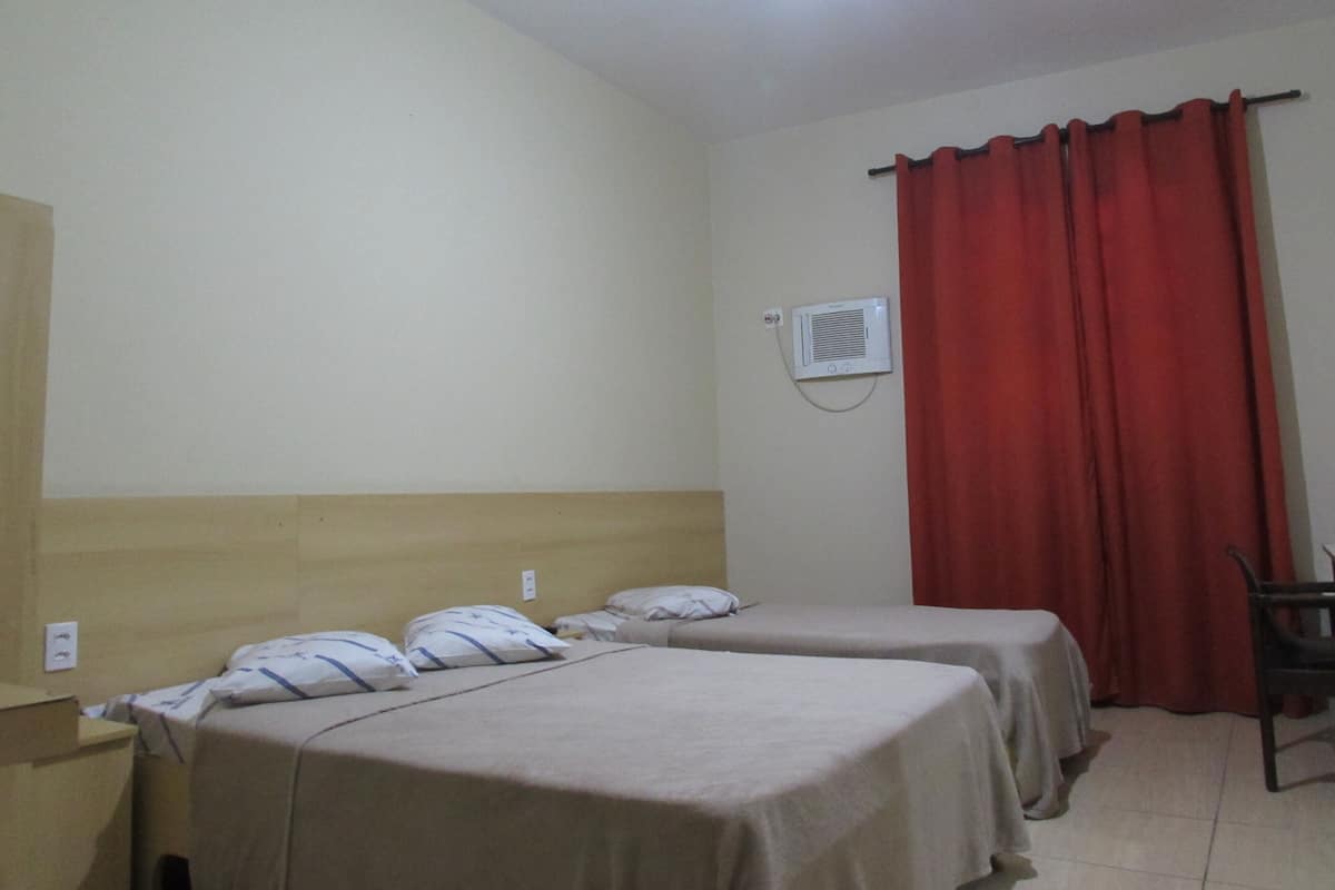 Une chambre d’hôtel avec deux lits simples, un rideau rouge, une petite table et un luminaire au plafond.